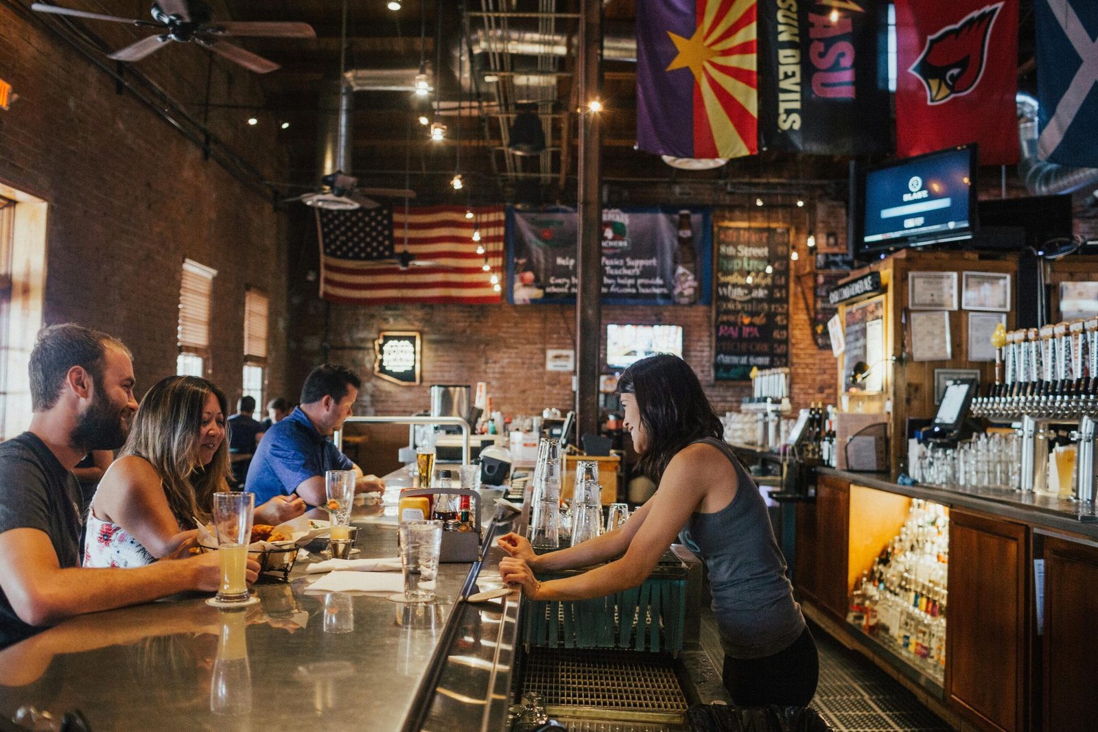 Group of friends enjoying drinks at a cozy bar with an American flag backdrop.